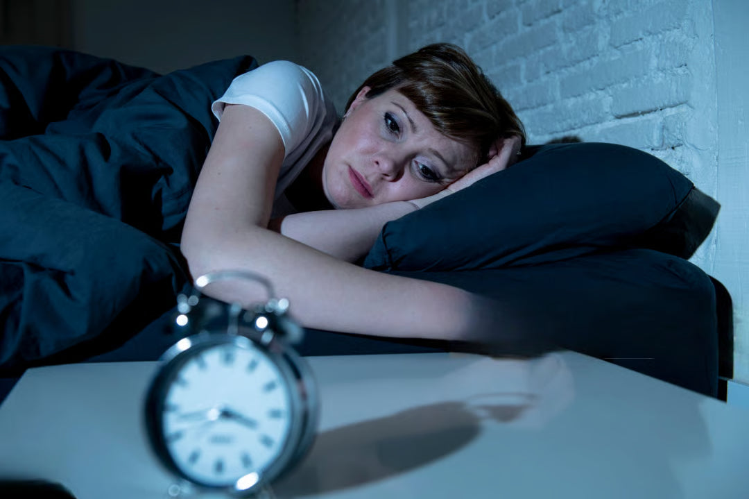 A woman lying awake in bed at 2 AM, an alarm clock in the foreground